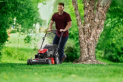 CRAFTSMAN CM12AVB2C2093 red and black lawn mower in use on grass near a tree, outdoor setting.