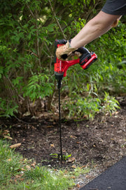 Photo of CRAFTSMAN CMCAWA cordless auger in use outdoors, drilling into soil near bushes, red and black design visible.