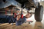 Photo of a person using a Craftsman CMCF920B cordless impact wrench under a vehicle, working on bolts in a garage.