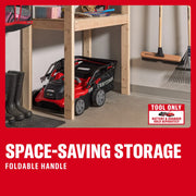 Craftsman lawn mower CMCOE210B with foldable handle, stored under a wooden shelf in a garage, angled side view.