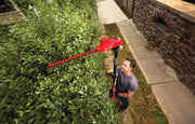 Photo of a person trimming a tall hedge with a red CRAFTSMAN pole hedge trimmer, SKU CMCPHT818D1, outdoors.