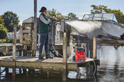 Photo of a person using a red CRAFTSMAN CMCPW1500N2 pressure washer to clean a boat on a dock by the water.