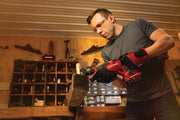 Photo of a person using a Craftsman cordless reciprocating saw, SKU CMCS300B, cutting a wooden board in a workshop.