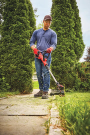 Photo of person using CRAFTSMAN string trimmer CMCST900B to edge grass along a sidewalk in a yard.