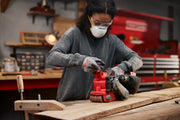 Person using a Craftsman cordless belt sander, SKU CMCW223B, on a wooden plank in a workshop setting.
