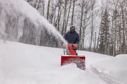 Photo of a person using a red Craftsman snow blower outdoors, SKU CMGB223104, clearing snow from a driveway.