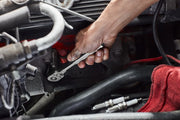 Close-up of a hand using a wrench to work on a car engine, with spark plugs and a red cloth nearby.