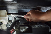 A close-up of a hand using a ratchet wrench to tighten a bolt inside a car engine compartment.