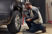 Photo of person using CRAFTSMAN lug wrench SKU CMMT98342 to loosen a car wheel nut in a garage setting.