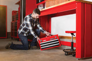 Photo of Craftsman red metal toolbox CMST27200R with black drawers, being placed under a red workbench in a garage.