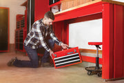 Photo of a person placing a red Craftsman tool chest, SKU CMST98245RB, with two drawers under a red workbench in a garage.