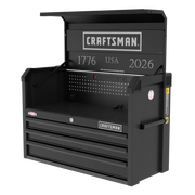 A black Craftsman-branded metal tool chest with three drawers, a hinged top lid, side handle, and built-in power strip. The interior back panel features the text '1776 USA 2026' and a perforated panel for organizing tools.