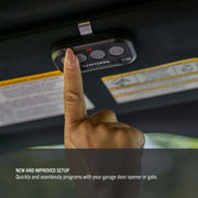 Photo of a hand pressing a button on a Craftsman garage door remote, CMX363, installed on a car ceiling.