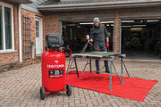 Photo of Craftsman air compressor CMXECXM331 on wheels outdoors, connected to a spray gun used for painting on a red tarp.