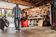 Photo of person pulling a red Craftsman wet/dry vacuum, SKU CMXEVBE17596, inside a garage workshop.