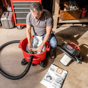 Photo of a Craftsman wet/dry vacuum, SKU CMXEVBE18595, with a person installing a filter bag into the red canister in a workshop.