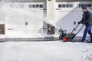 Photo of CRAFTSMAN snow blower CMXGBAM1054539 in use clearing snow from a driveway in front of garage doors.