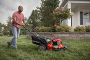 Photo of a person using a Craftsman lawn mower, SKU CMXGMAM221101, on a grassy lawn in front of a house.