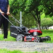 A person is pushing a red and black CRAFTSMAN lawn mower on a grassy area outdoors, surrounded by trees and greenery.
