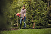 Photo of a person using a Craftsman string trimmer CMXGTAMDCS25 outdoors on grass, with trees in the background.
