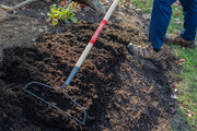 Photo of a CRAFTSMAN garden rake, SKU CMXMLTP35315, metal head and wood handle, in use spreading soil outdoors.