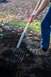 Photo of a person using a CRAFTSMAN garden fork, SKU CMXMLTP35326, with wood handle, turning soil outdoors.