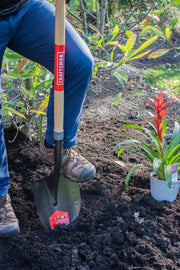 Photo of Craftsman shovel CMXMLTP35329 digging soil near potted red flower, used for gardening outdoors.