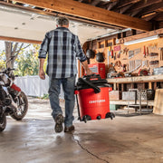 Photo of a person carrying Craftsman wet/dry vacuum, SKU CMXZVBE37035, in a garage workshop with tools on the wall.