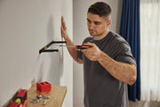 A person uses a CRAFTSMAN screwdriver to install a black metal wall bracket. The face of the person is blurred. Tools and hardware are placed on a nearby wooden surface.
