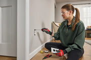 Person wearing gloves is using a CRAFTSMAN screwdriver to work on an electrical outlet on a wall. Other tools and outlet components are placed on the floor nearby.
