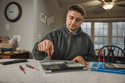 A person using a CRAFTSMAN precision screwdriver to repair a laptop on a kitchen counter, with additional screwdrivers and