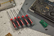 Five CRAFTSMAN precision screwdrivers with black and red handles are arranged on a work surface next to an open electronic