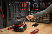 A CRAFTSMAN workshop with hand tools hanging on a pegboard, a battery charger on a workbench, and a person plugging in a USB